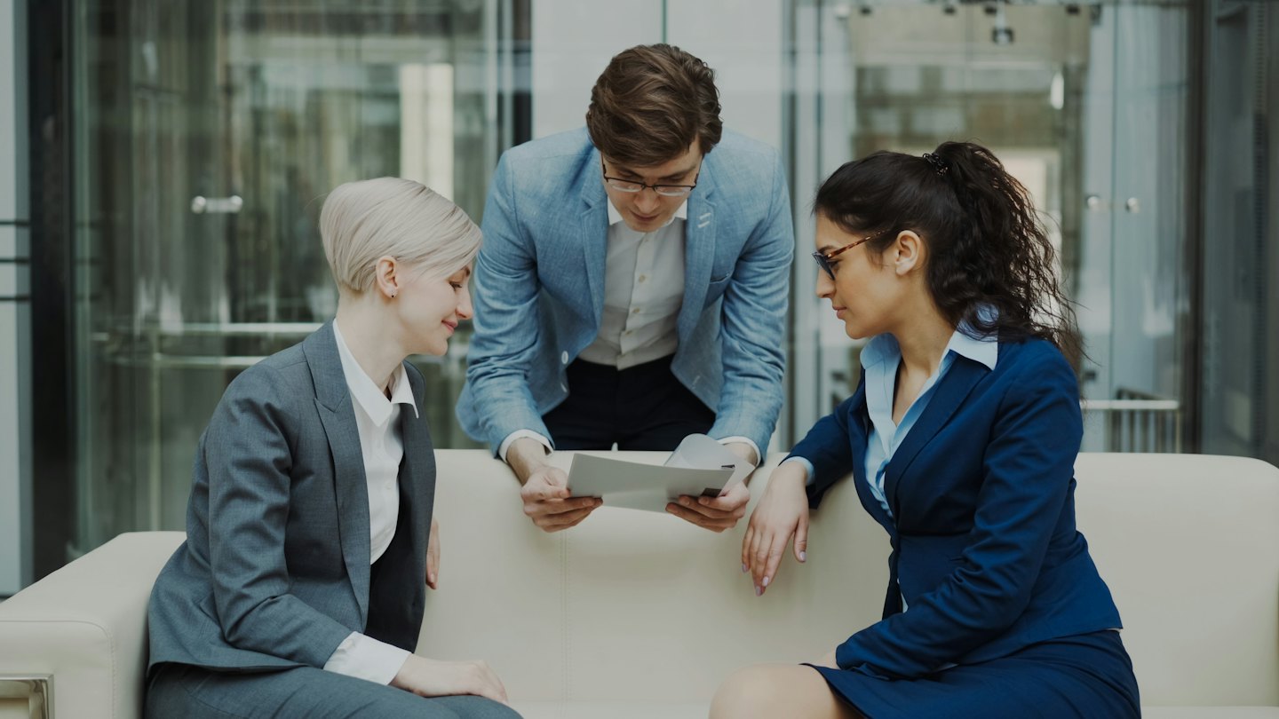 Diverse business team discusses documents on a modern office sofa.
